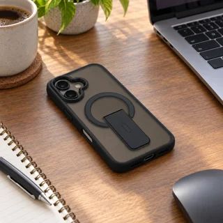 قاب دودی پایه‌دار برلیا مشکی iPhone 16 خوابیده روی میز کار کنار لپ‌تاپ